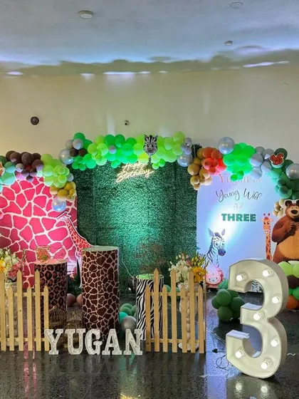 A vibrant jungle safari theme, perfect for a wild third birthday party. This setup features a lush green backdrop, fun animal cutouts like a tiger and elephant, a large light-up marquee number '3', and custom plinths with animal prints.