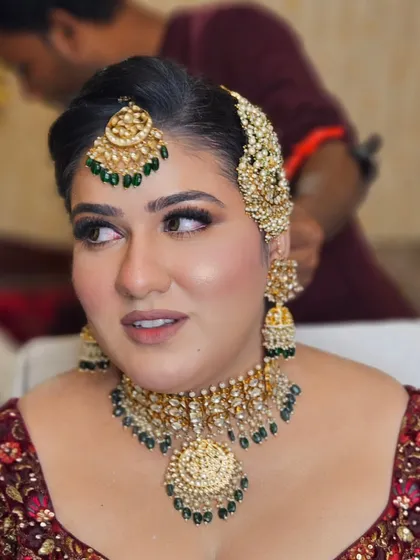 A close-up of the makeup and jewelry. The gold and green kundan jewelry is paired with a soft gold shimmer on the eyes and a natural lip color.