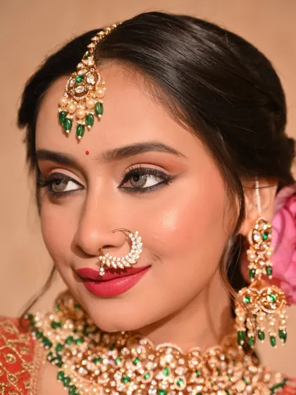 A close-up of a modern traditional look. The makeup features sharp winged eyeliner and a bold pink lip, with a lotus flower in the hair for a unique touch.