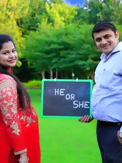 A happy couple posing with a "He or She" sign during their outdoor maternity shoot. This is a great way to create photos for a gender reveal.