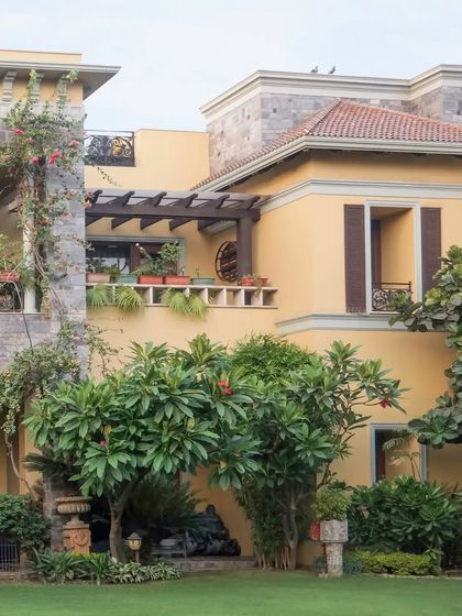 Another view of the European-inspired residence, highlighting the stone cladding, pergola, and shuttered windows that contribute to its classic, warm aesthetic.