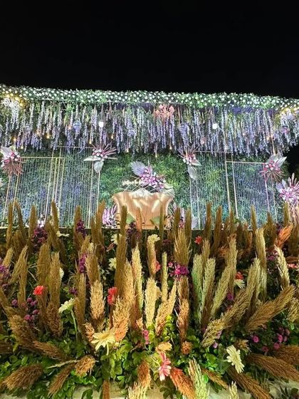 A truly stunning night wedding decor concept. We layered pampas grass, vibrant florals, and hanging crystal elements against a green wall, using dramatic lighting to create a magical, multi-textured effect.