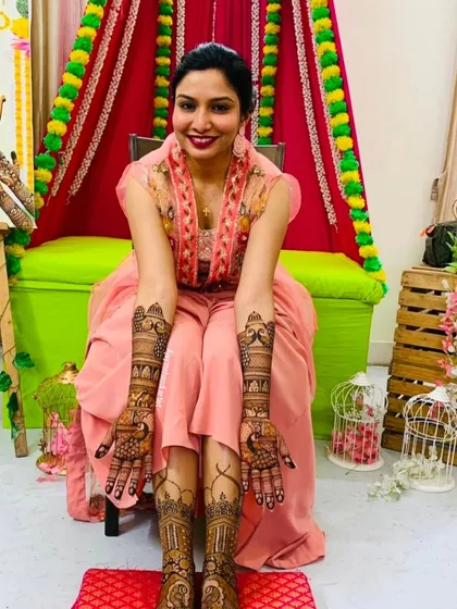 A happy bride displaying her full bridal mehndi. The designs on her hands and feet are intricate and perfectly matched for her wedding day.