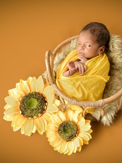 This 15-day-old newborn is wrapped in a vibrant yellow, complemented by sunflowers. This shot shows how a pop of color can create a bright and joyful portrait while the baby remains comfortably posed.