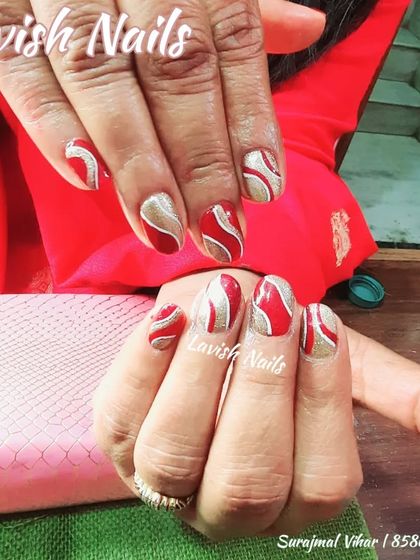 A festive red and gold glitter manicure with a swirling, abstract pattern.