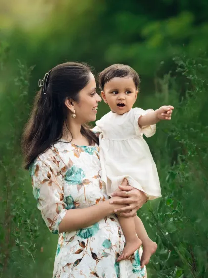 A mother holds her baby girl, who is pointing at something with wonder. This candid moment was captured during a beautiful outdoor sitter session.