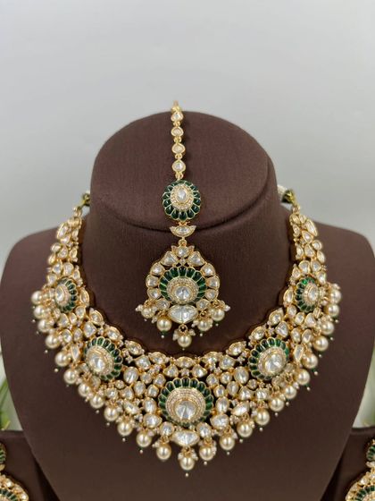 The Zarista Premium Moissanite Necklace set, shown here in both ruby and green variations. This set includes a necklace, maang tikka, and earrings, featuring large central stones surrounded by detailed craftsmanship.