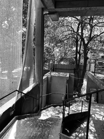 A view of an exterior staircase during construction, with natural light creating strong shadows on the unfinished concrete structure.