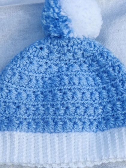 A complete newborn baby winter set in soft blue and white yarn. The set includes a cozy cardigan, pants with a drawstring, a pom-pom hat, and adorable little booties.