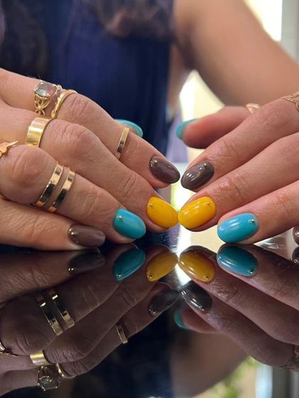 An eclectic and colorful manicure with a mix of brown, turquoise, and yellow nails.