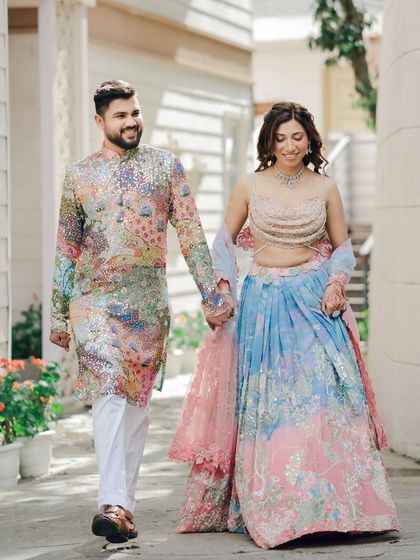 The couple walks hand-in-hand through a picturesque lane. Their colorful Mehendi outfits and happy expressions make for a perfect pre-wedding portrait.