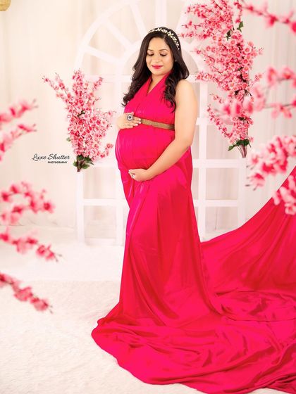 This full-length portrait showcases the beautiful drape of the pink satin gown against a soft, floral backdrop. The tiara adds a touch of regal elegance.