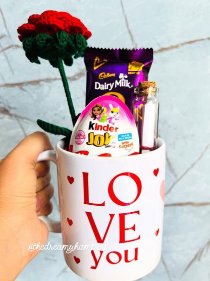 A sweet and budget-friendly Valentine's gift. This "Love You" mug is filled with a handmade crochet rose, Kinder Joy, Dairy Milk chocolate, and a tiny message in a bottle.