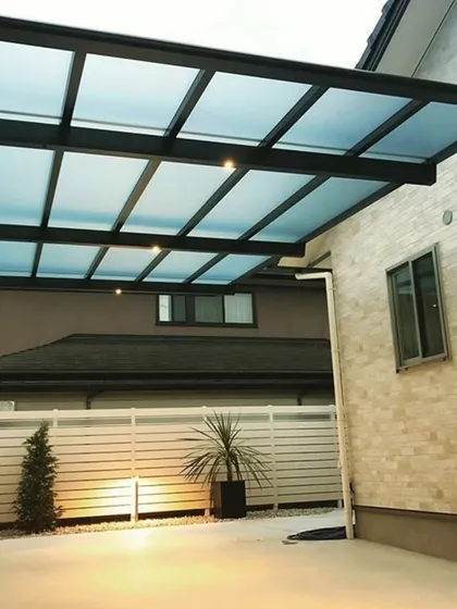 This modern carport features a translucent polycarbonate roof and a minimalist black frame. The design provides shelter for the vehicle while allowing light to pass through, preventing the area from feeling dark.