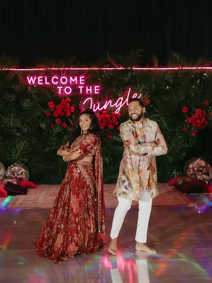 Welcome to the jungle! The couple's playful pose in front of the neon sign captures the fun and energy of their Sangeet night, with their outfits perfectly matching the theme.