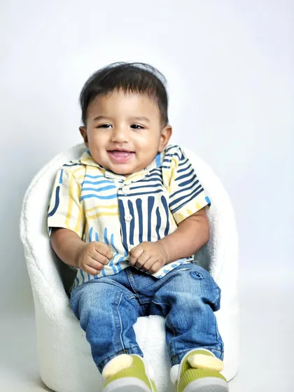 A happy, smiling portrait of one of the twin boys. Using a simple white chair and background keeps the focus entirely on his joyful expression.