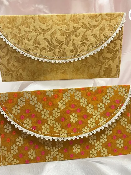 A pair of our elegant brocade envelopes, one in a classic gold and the other in a vibrant mustard yellow floral pattern.