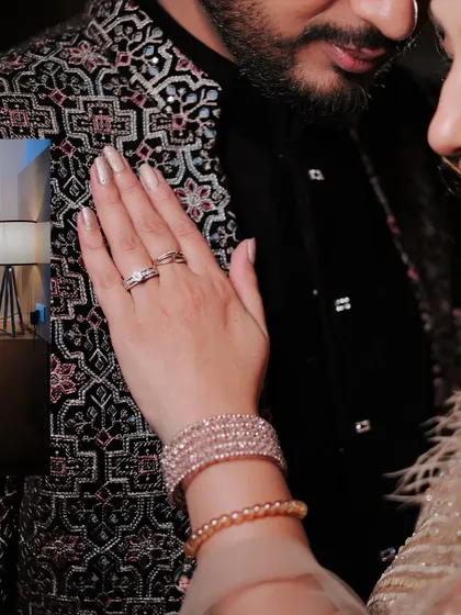 A close up detail shot focusing on the bride's hand on the groom's intricately designed jacket, showcasing her ring and bracelets.