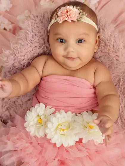 A sweet four-month-old baby girl in a pink tutu, surrounded by flowers. Her gentle smile is just heart-melting.