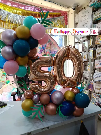 A compact tabletop balloon arrangement for a 50th birthday, featuring a small ring frame and rose gold number balloons.