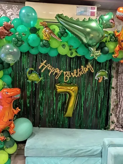 A prehistoric party with a dinosaur theme. This room decoration uses a green foil curtain and a balloon arch with various dinosaur foil balloons to create a jungle-like atmosphere for a 7th birthday.