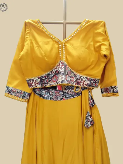 A close-up of the yellow lehenga's blouse, featuring a V-neckline with delicate mirror work and printed fabric accents on the waist and sleeves.