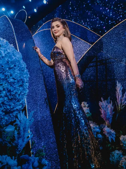 The bride stands amidst the decor, where glittering blue panels and soft, ethereal florals in shades of blue and lavender come together to create a dreamy, celestial photo corner.