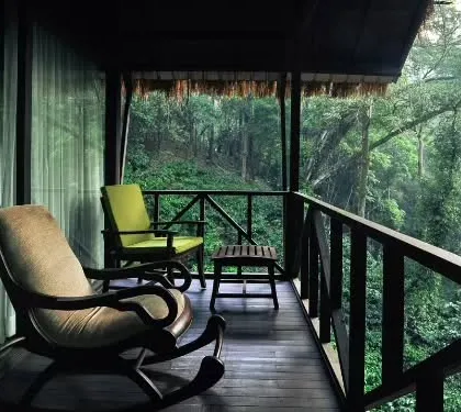 A rocking chair on the balcony of a lodge in Coorg, overlooking a dense forest valley. This is the ideal spot to sit back, relax, and listen to the sounds of nature.