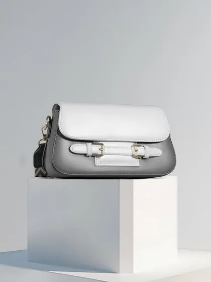 A minimalist composition featuring a grey and white handbag on a white block. The clean lines, simple color scheme, and balanced composition create a feeling of modern elegance and simplicity.