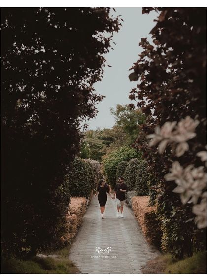 The couple walking down a path lined with manicured hedges, a serene and elegant pre-wedding shot.