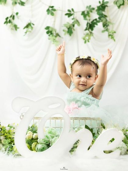 A beautiful first birthday portrait. This baby girl celebrates turning one in a whimsical setup with white and green floral decorations.