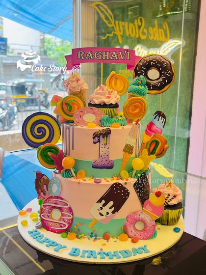 A candyland dream cake for Raghavi's first birthday. This two-tier cake is loaded with edible decorations like donuts, lollipops, ice cream cones, and colorful sprinkles.