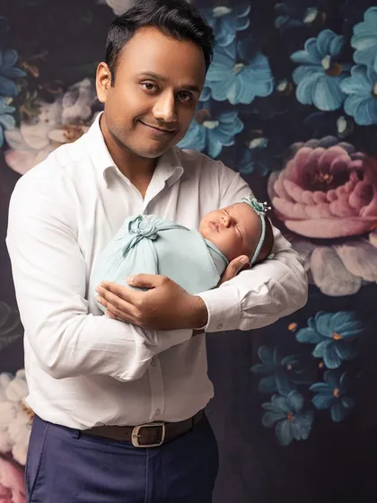 A proud father holds his newborn daughter. The floral background adds a soft, artistic touch to this classic daddy-and-me portrait.