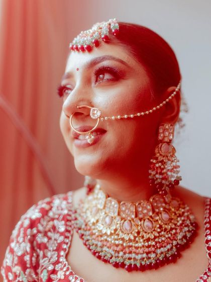 A close-up portrait of a bride, capturing her happy expression and beautiful jewelry. The warm, reddish tint adds a unique artistic touch to the photo.