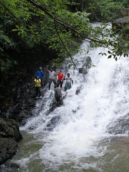 A group of trekkers enjoying a playful moment on the rocks of a cascading waterfall during our monsoon road trip.