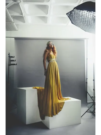 A full shot of the golden Rudraksh Dwivedi gown, revealing the studio setup. This type of image gives a glimpse into the process while still showcasing the fashion beautifully.