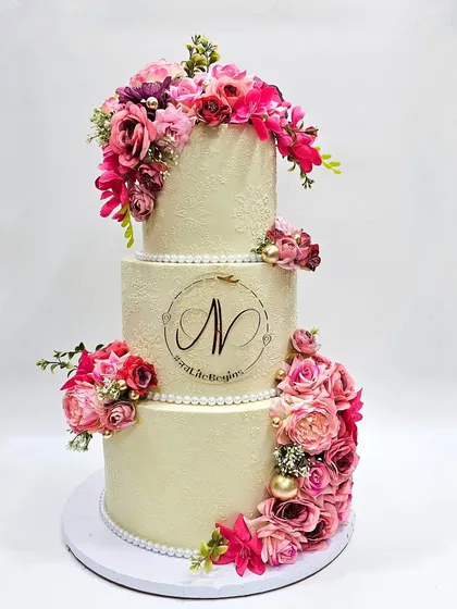 A beautiful three-tier wedding cake with a cascade of pink and magenta flowers. The delicate lace stenciling on the buttercream adds a touch of classic elegance.