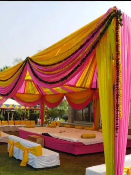 A colorful outdoor mandap with yellow and pink drapes and low seating arrangements, designed for a traditional daytime ceremony.