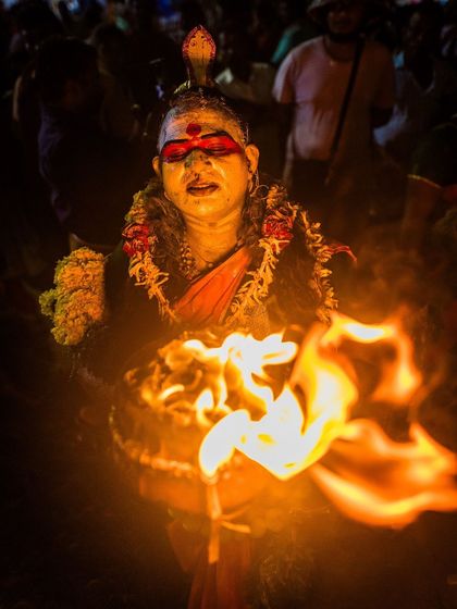 A devotee holds a bowl of fire, the flames illuminating their face in the darkness, symbolizing a powerful act of faith and ritual.