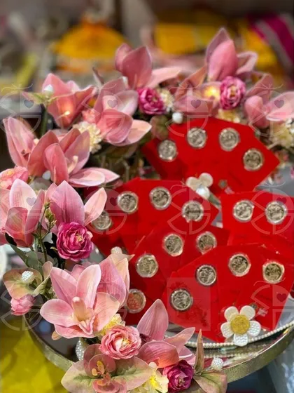 A beautiful platter for presenting shagun coins. The red velvet holders are arranged on a silver tray and adorned with delicate pink orchids, creating a luxurious and traditional display.