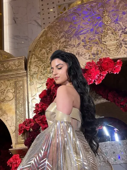 The bride looks like a goddess in her metallic gown, with her hair styled in long, flowing waves that add to the drama of the look.