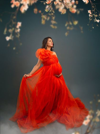A fiery and passionate portrait. The vibrant red tulle gown and the mother's serene expression create a stunning contrast, framed by delicate blossoms for a touch of softness.