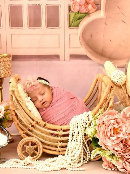 A baby girl in a pink wrap sleeps in a wicker pram, surrounded by a vintage-inspired setup with flowers, pearls, and lanterns. This theme is perfect for a classic, elegant look.