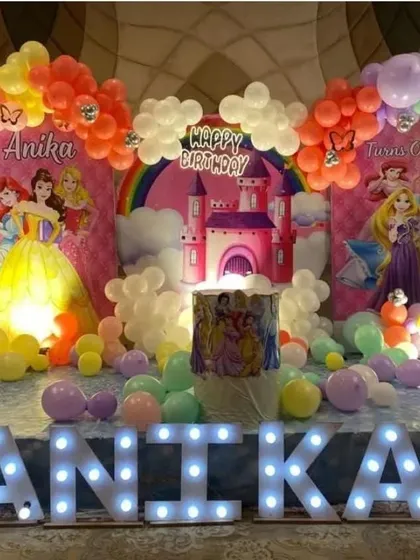 A Disney Princess castle theme for a first birthday. This stage decoration includes a large backdrop, marquee letters, and a colorful balloon arch.