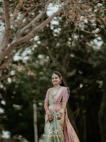 The bride smiling in a beautiful outdoor setting, her pastel saree blending perfectly with the natural light.