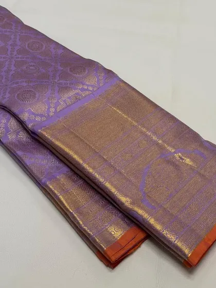 A folded view of a pure Kanchi Pattu silk saree in a lovely lavender shade with a gold and orange border. The quality of the silk and zari is evident.