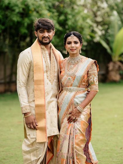 A portrait of a couple with their son, all in coordinated outfits. The father and son wear matching cream and gold dhoti-kurtas, while the mother's pastel saree complements the look perfectly.