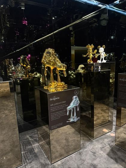 This installation showcases sculptures that elevate everyday objects into art. The golden 'Air Jordan Drip' and KAWS-style figures on mirrored pedestals reflect our interest in sneaker culture and collectible design.