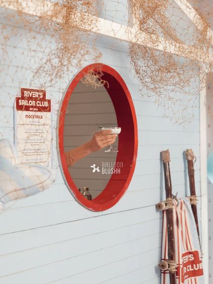 A guest's hand reaches through the porthole of the sailor cabin to grab a mocktail, a fun and interactive detail.