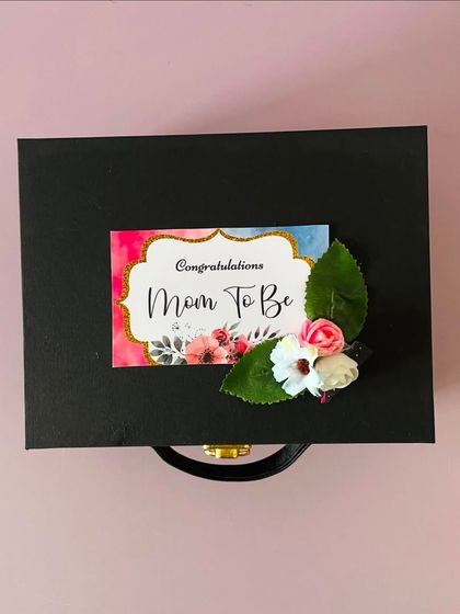 A closed view of the "Mom To Be" hamper, showing the custom tag on the black suitcase box. The presentation is just as important as the gifts inside.